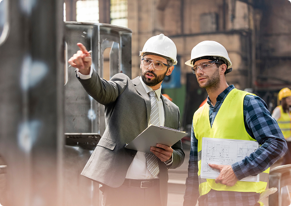 Engineers in hard hats reviewing plans at a manufacturing facility